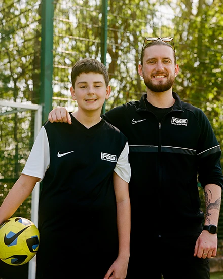 Smiling man with his arm around a young boy, both standing side by side and looking at the camera
