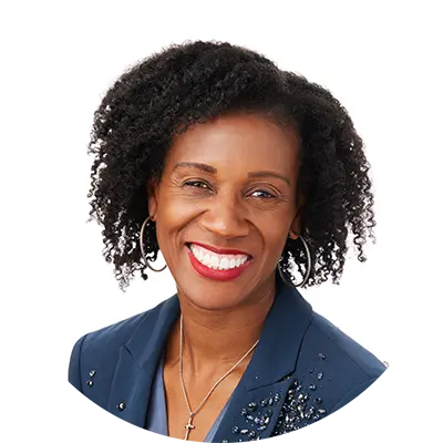 A black woman with short, dark curly hair smiles. She wears a blue blouse and a dark blue jacket.