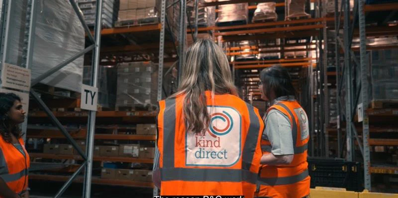 Two warehouse workers wearing safety vests with In Kind Direct logo on the back.