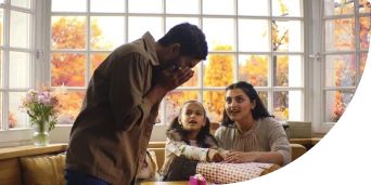 Man sneezing in front of his wife and little daughter while they wrap presents