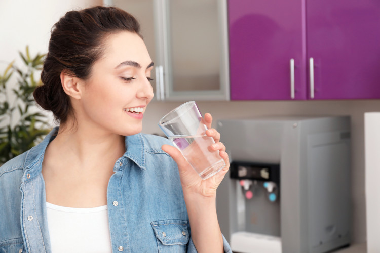 To avoid getting a headache, a young woman drinks water to stay hydrated.