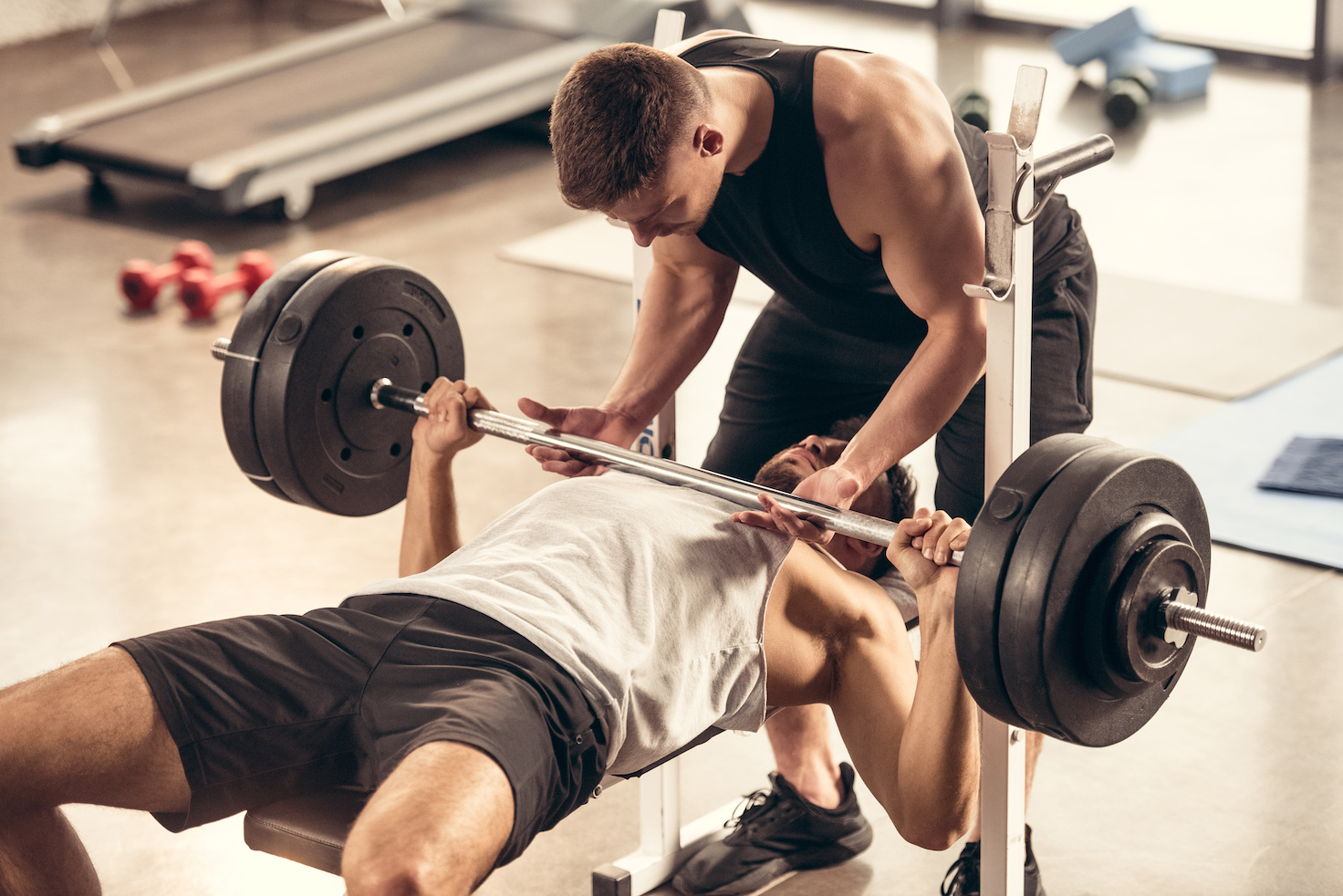 A person being supervised by a coach while performing a basic weight lift/press.