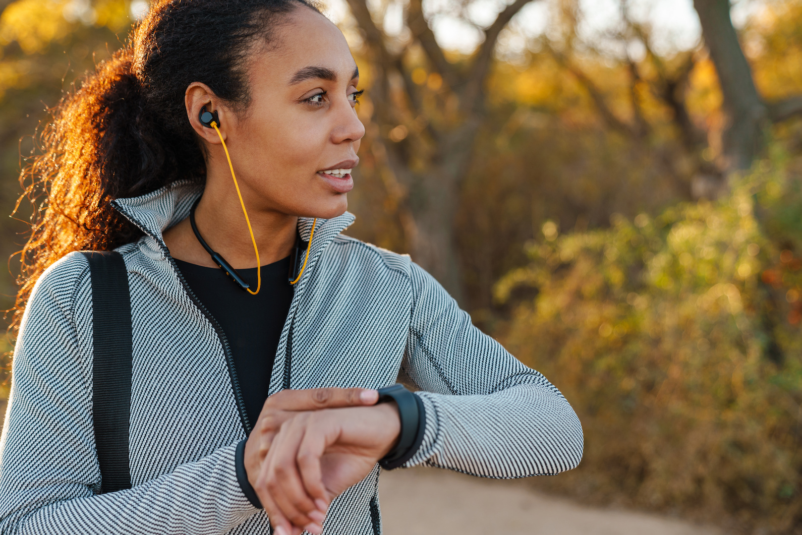 Woman with headphones on, outside checking her fitness watch