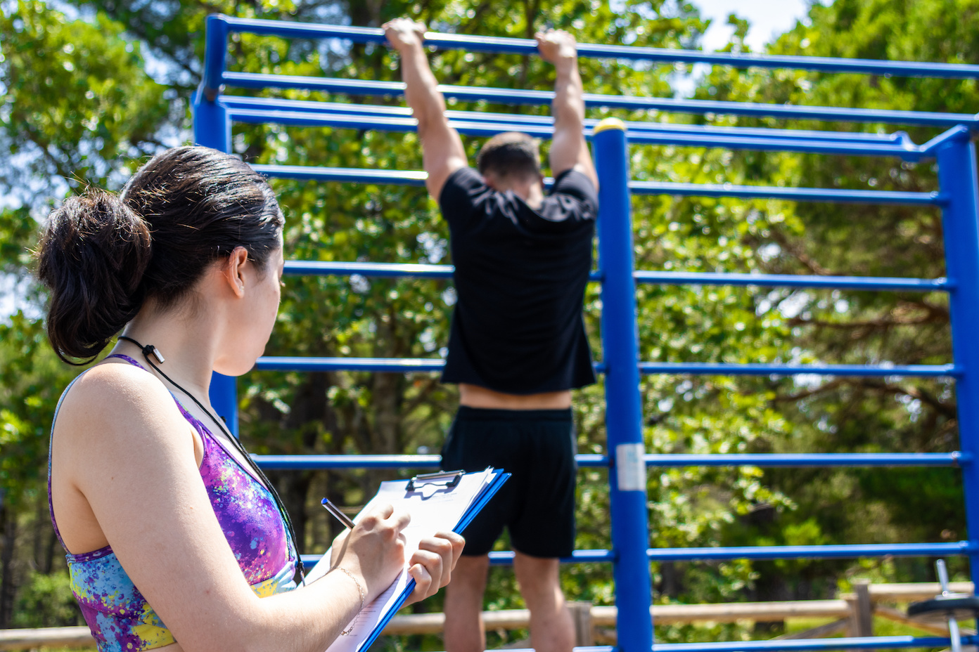 A person being supervised by a coach while maintaining a strenuous, muscular hold such as a pull up.