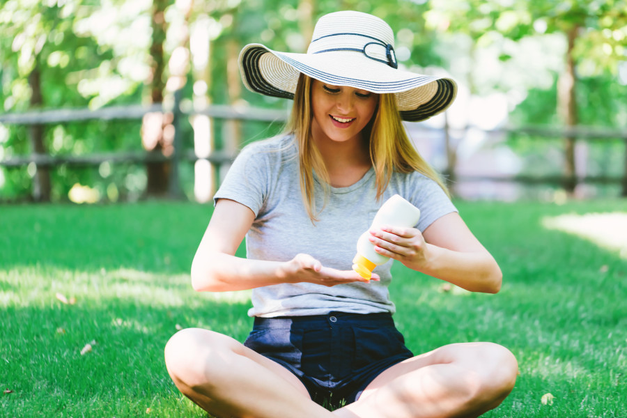 A woman wearing a sun protection hat and applying sunscreen to protect against UVA and UVB rays before her walk in the park.
