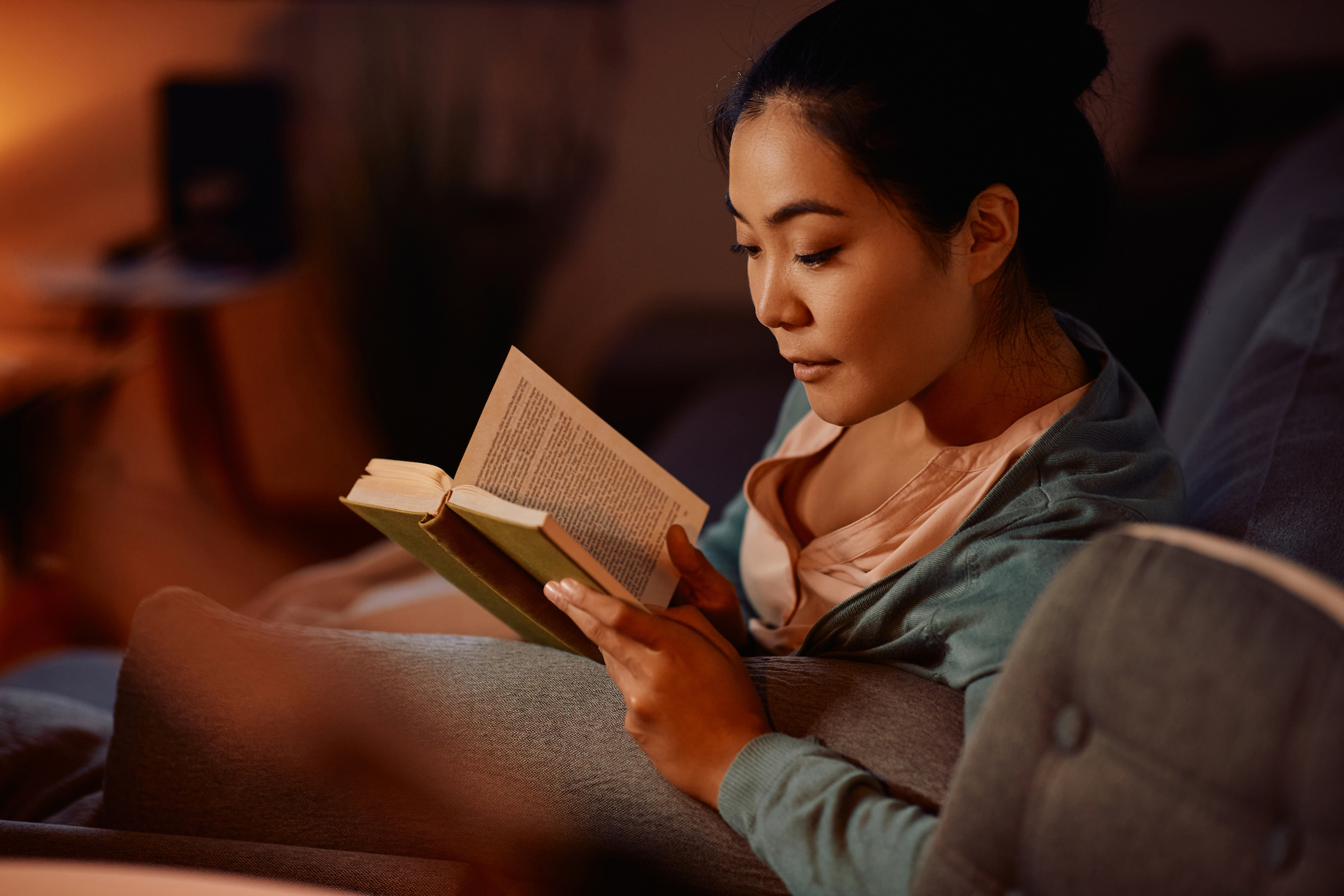 Woman reading a book at night in a dimly lit room.