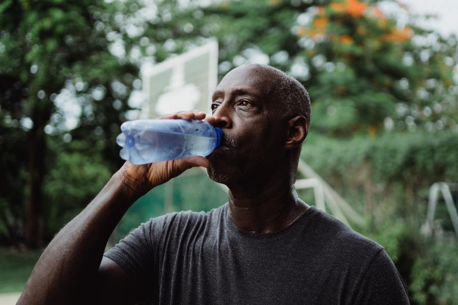 A man drinking from a water bottle to stay hydrated during his outdoor summertime workout session.