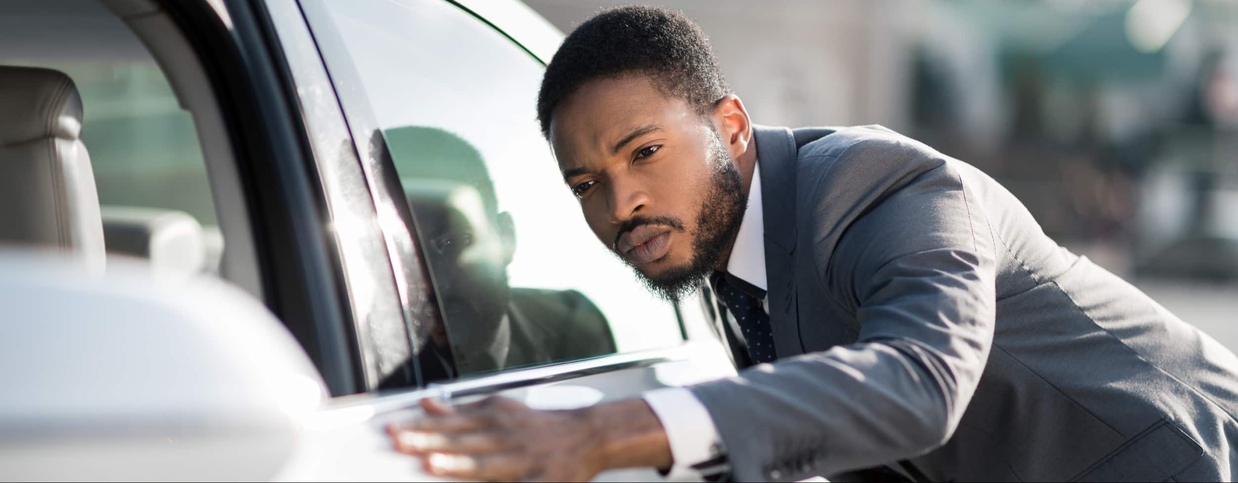 A salesperson wearing a suit checks the outside of a car.