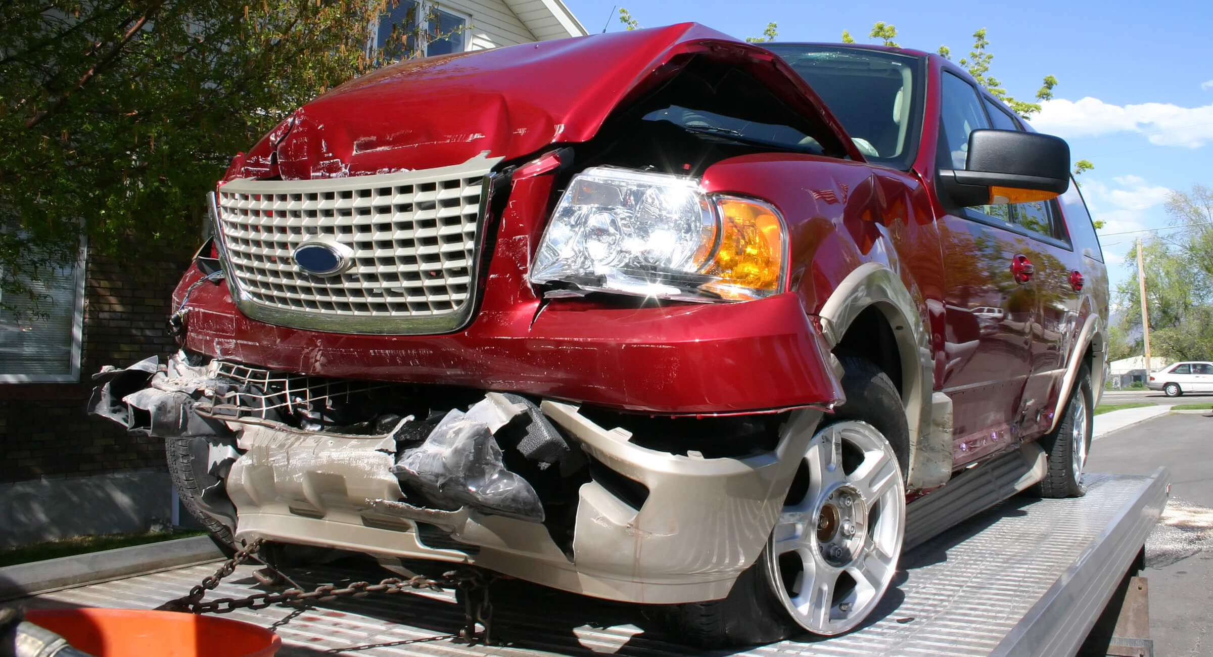 Red car with a damaged front end sits on a tow truck.