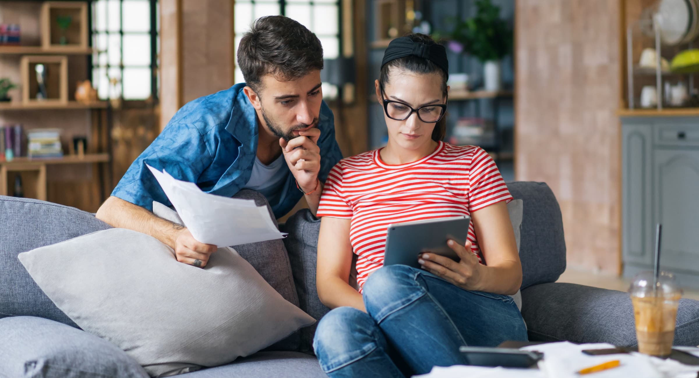 A young couple looking at a tablet and holding paperwork as they compare auto loan options.