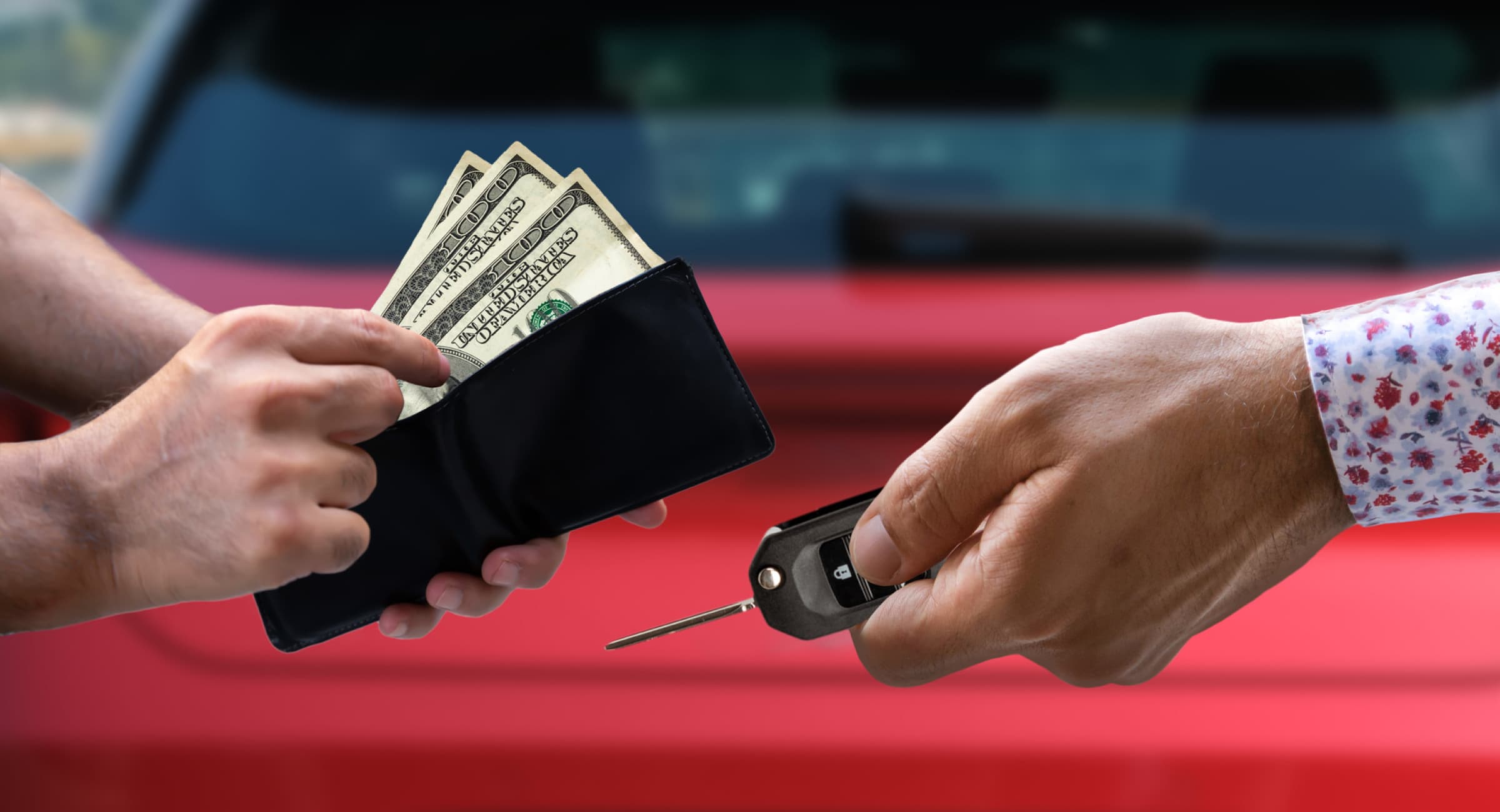 Close up of a hand holding out a car key while two other hands take cash out of a wallet during a car sale. 