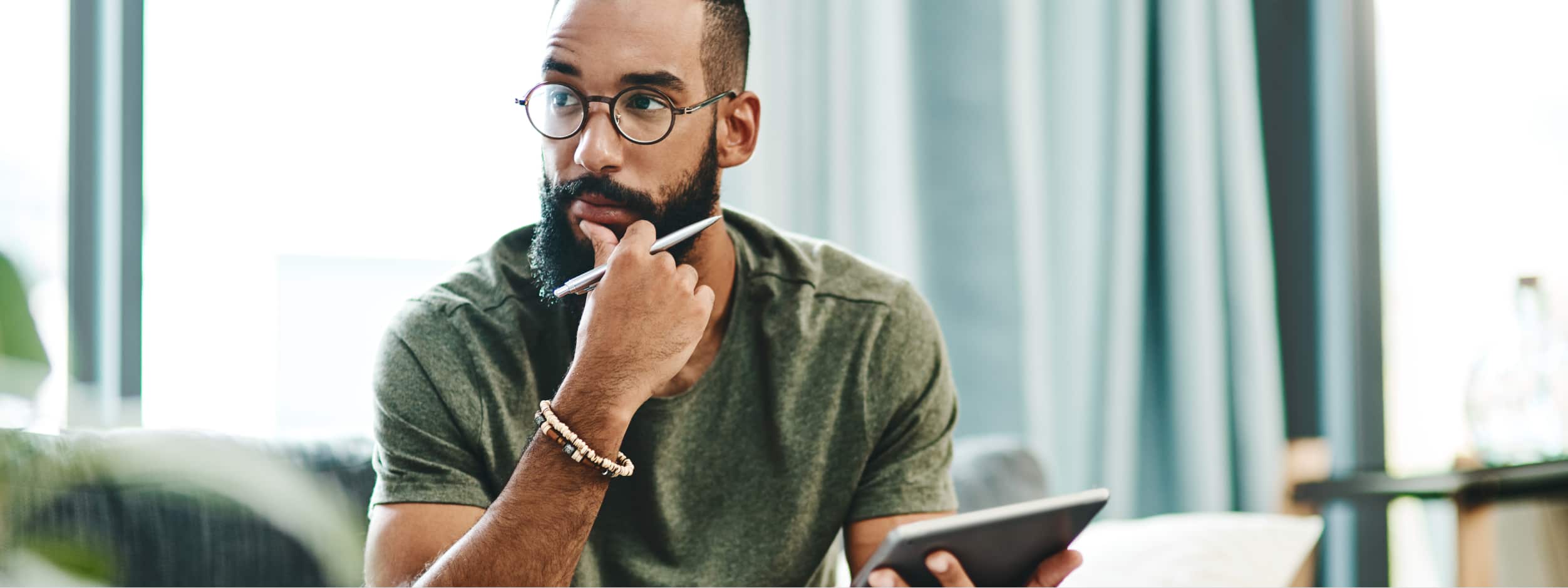 A man looks pensive while holding a phone and a pen. 