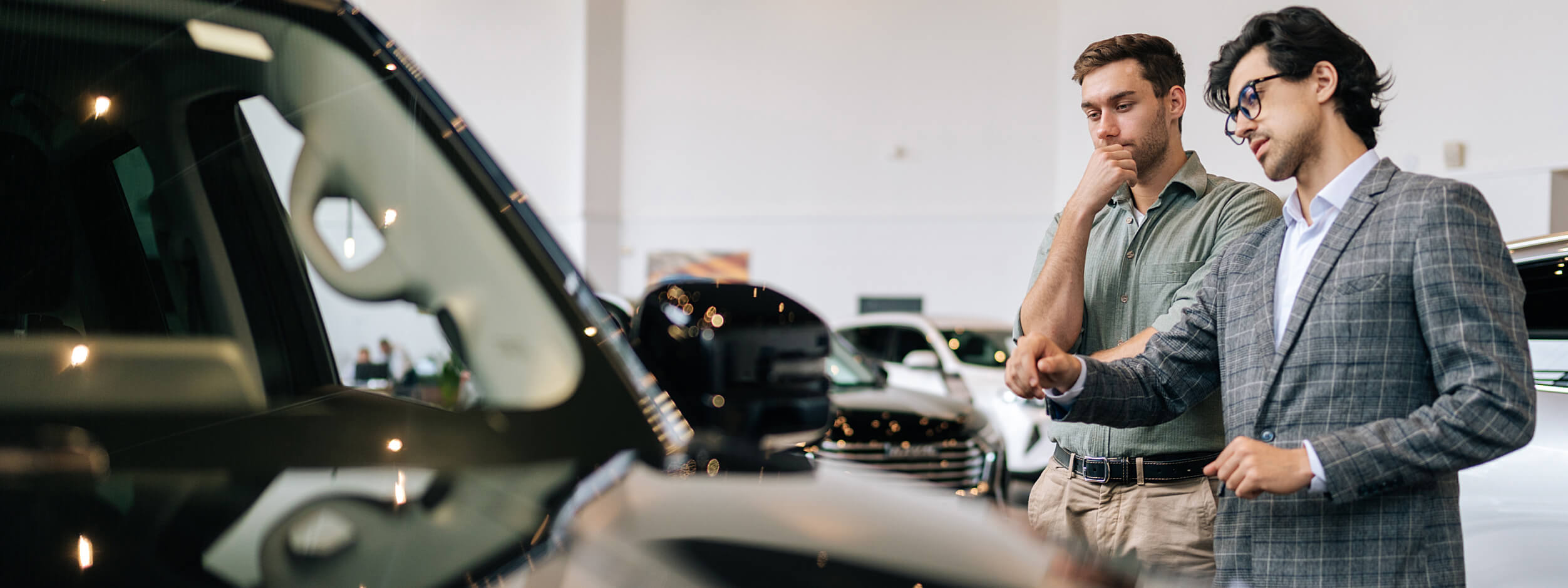 A buyer and salesperson look at a car in a showroom. 