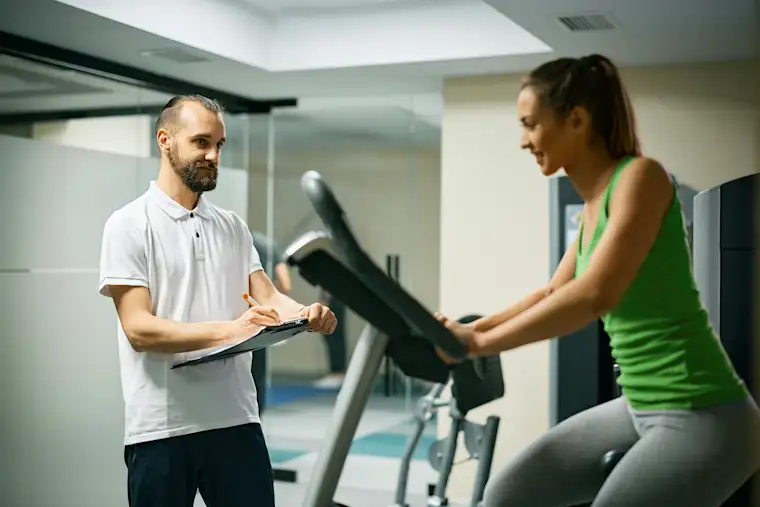 Beauty Wellbeing And Sport - Landscape - Cycling Coach - Hero - Cycling coach taking notes while client is training