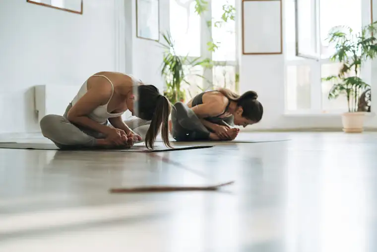 Beauty Wellbeing And Sport - Landscape - Yoga Instructor - Hero - Two women in childs pose in bright studio