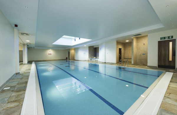 Sizeable indoor swimming pool with pale stone edges and a shower at one side