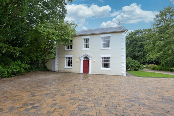 The exterior of a large detached property. A cream Georgian Grade II listed house sits behind a large brick driveway