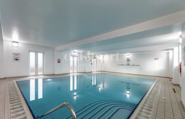 A large indoor pool which is almost totally square, with pale surrounding tiles and white walls 