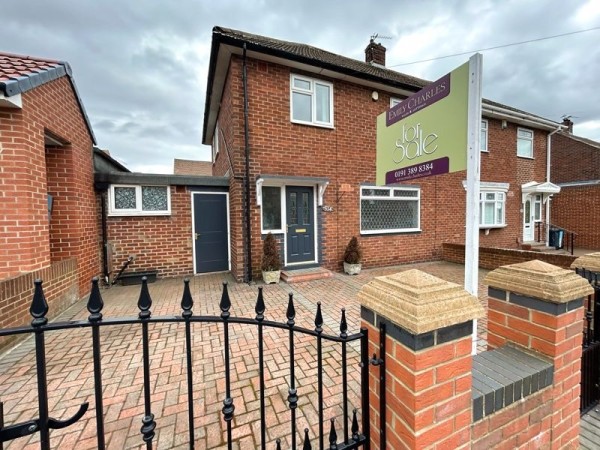 A three bed semi-detached house with a large bricked driveway in front. There is a dark front door, a wrought iron gate to the drive and a 'For sale' sign at the entrance.