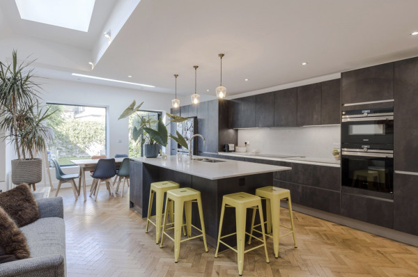 Modern kitchen with grey units, white worktops, wooden floors, a skylight and yellow stools