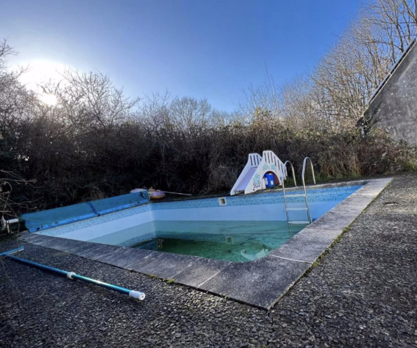 An outdoor swimming pool with a children's slide, surrounded by concrete and in need of a clean 