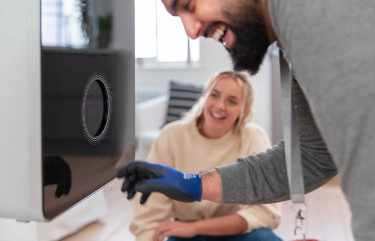 A man laughing while installing a new boiler as a woman laughs in the background