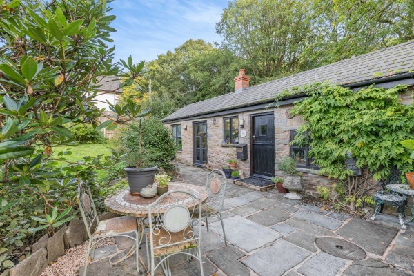 A single storey detached annexe converted from former barn outbuildings. The stone building has a black stable door and the patio has vintage furniture and greenery all around.