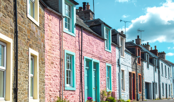 A row of characterful and colourful terraced houses, looking down the street as they continue to the distance. They're set close to the road and there's a sunny blue sky above