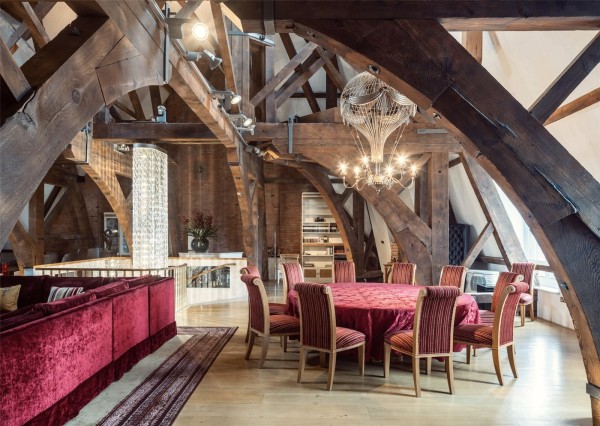 The interior of a penthouse at St Pancras Chambers with dramatic Victorian beams that separate the huge room. There is a large round dining table with red cloth and red chairs.