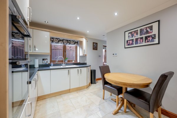 A square shaped kitchen in the annexe with cream units, a two-person dining table with brown leather chairs, light tiled flooring and fitted applicances.