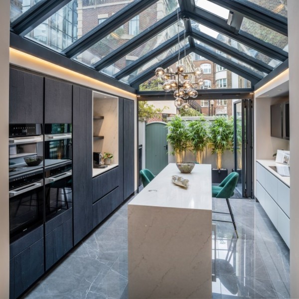 An architecturally designed kitchen with black built-in cabinets, a pitched glass ceiling and an island with full height doors to the garden.