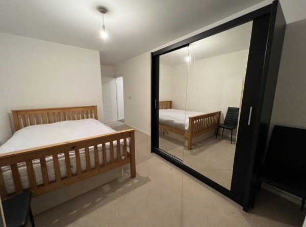 The bedroom of a two-bed flat for sale on Zoopla. The small double room has a wooden double bed with a mattress and a black double wardrobe with mirrors.