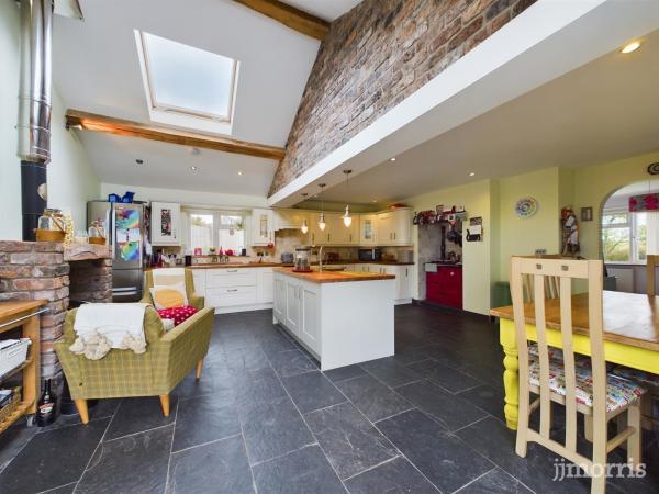 A large kitchen with flagstone flooring, high ceilings with sky lights, country-style units and island and a cosy sofa in front of a brick fireplace