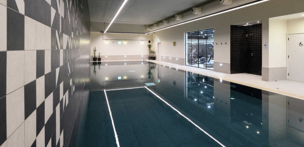 Stylish indoor swimming pool with geometric tiles on one wall and showers at the sides