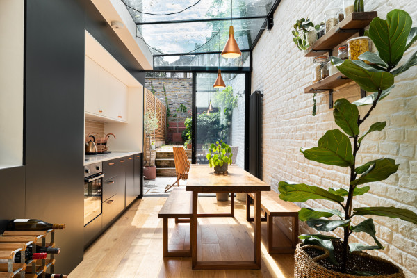 A stylish kitchen extension in industrial style with wooden flooring, brick walls and window skylights, with a large plant in the foreground and a dining table with benches
