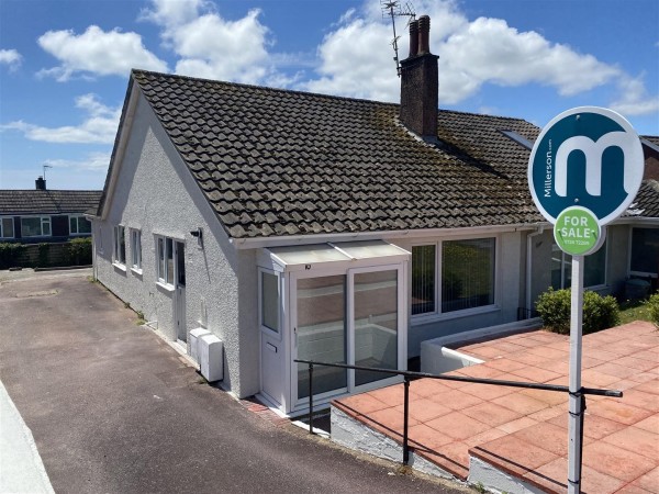 The exterior of a small bungalow for sale in Par. A tarmac driveway leads to the left of the house and a For Sale sign is in the foreground.