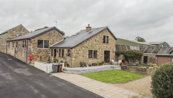 Exterior of an equestrian property in Burnley. The converted farmhouse looks modern from the outside and sits next to a newly tarmacked lane. There is a neat front garden with wraparound patio and seating.
