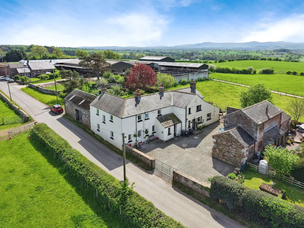 Aerial view of a large white farmhouse-style home with several outbuildings and surrounded by green fields
