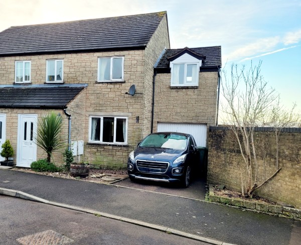 The exterior of a four bedroom semi for sale in Cinderford. It is built from Cotswold stone and has a porch and garage extension with a car parked in front.