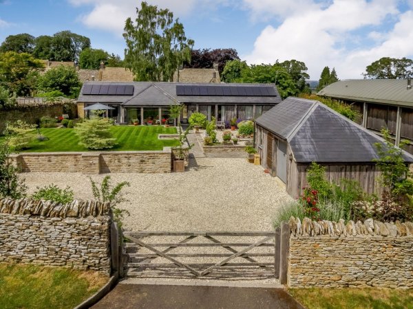 A modern eco home in the Cotswolds, where converted barn-style building with solar panels sits within landscaped gardens and has a gravel driveway.