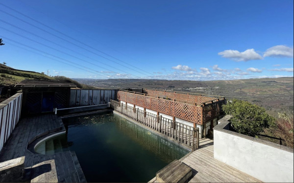 An outdoor swimming pool in need of a clean and a bit of TLC as the water is green, but with stunning views of the Welsh countryside