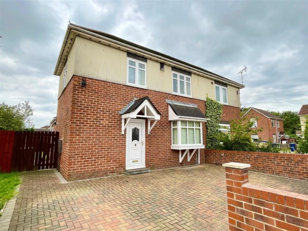 The exterior of a two bedroom semi-detached house. There is a large double driveway and a white front door with a gate giving side access to the rear garden.