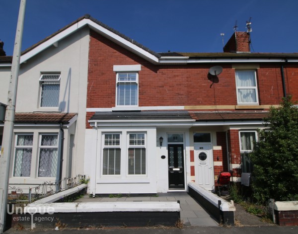 A terraced period property for sale in Fleetwood. The two-storey home has a small paved front garden, black front door and a red-brick upper half.
