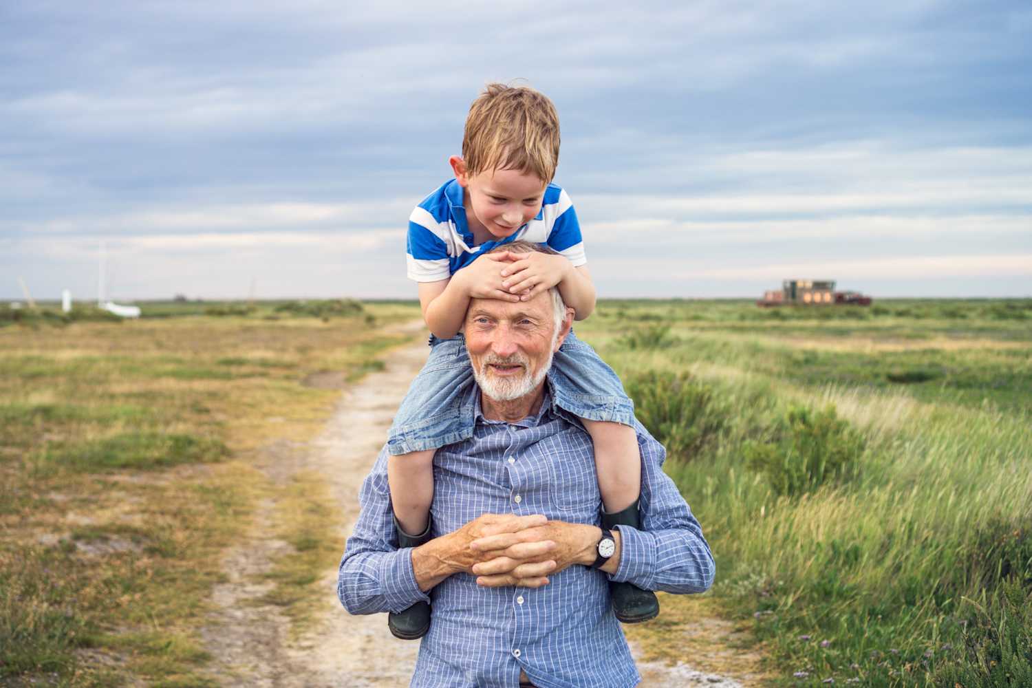 A grandad carrying his grandson on his shoulders by the beach