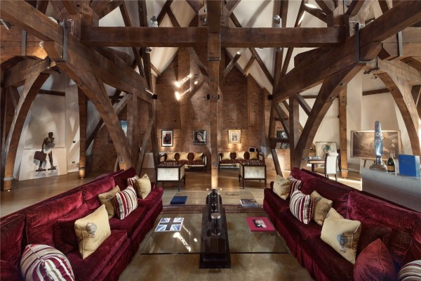 Another angle of the penthouse in St Pancras Chambers with its dramatic Victorian beams that come down at all angles from the super high ceiling. Two red velvet sofas face each other and glass coffee tables.