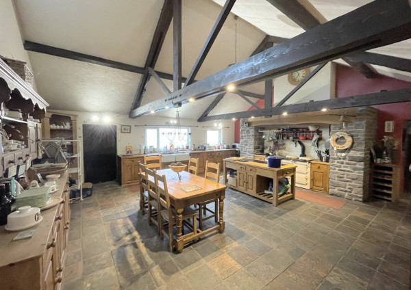 The interior of a spacious farmhouse kitchen with flagstone floor and exposed beams, a dresser, kitchen table and chairs and wooden worktops and kitchen island