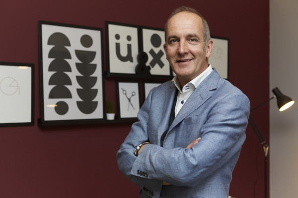 Kevin McCloud, presenter of Grand Designs, wearing a suit and standing in front of some art