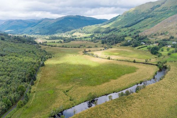 An expanse of land for sale in Scotland with a river running in the foreground, dramatic hills on either side and rugged scenery as far as you can see