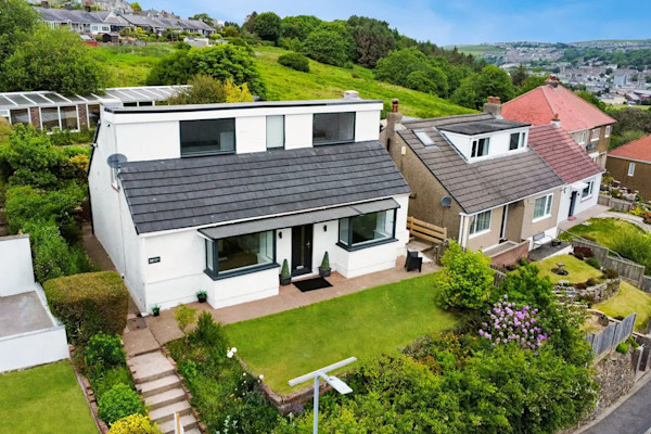 A modern detached house with white exterior perched on the side of a hill in Whitehaven, Copeland