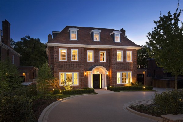 A large imposing detached home in Hampstead Gardens. A half-moon driveway leads to the front door. The photo is taken at dusk so windows are lit to create a welcoming look.